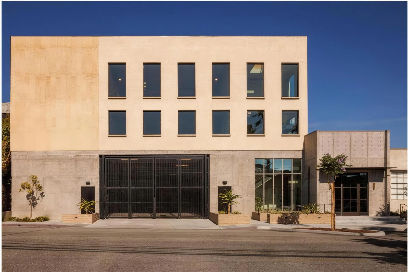 A new three storey building in plaster and board-formed concrete, with a steel gate and a glazed stair hall