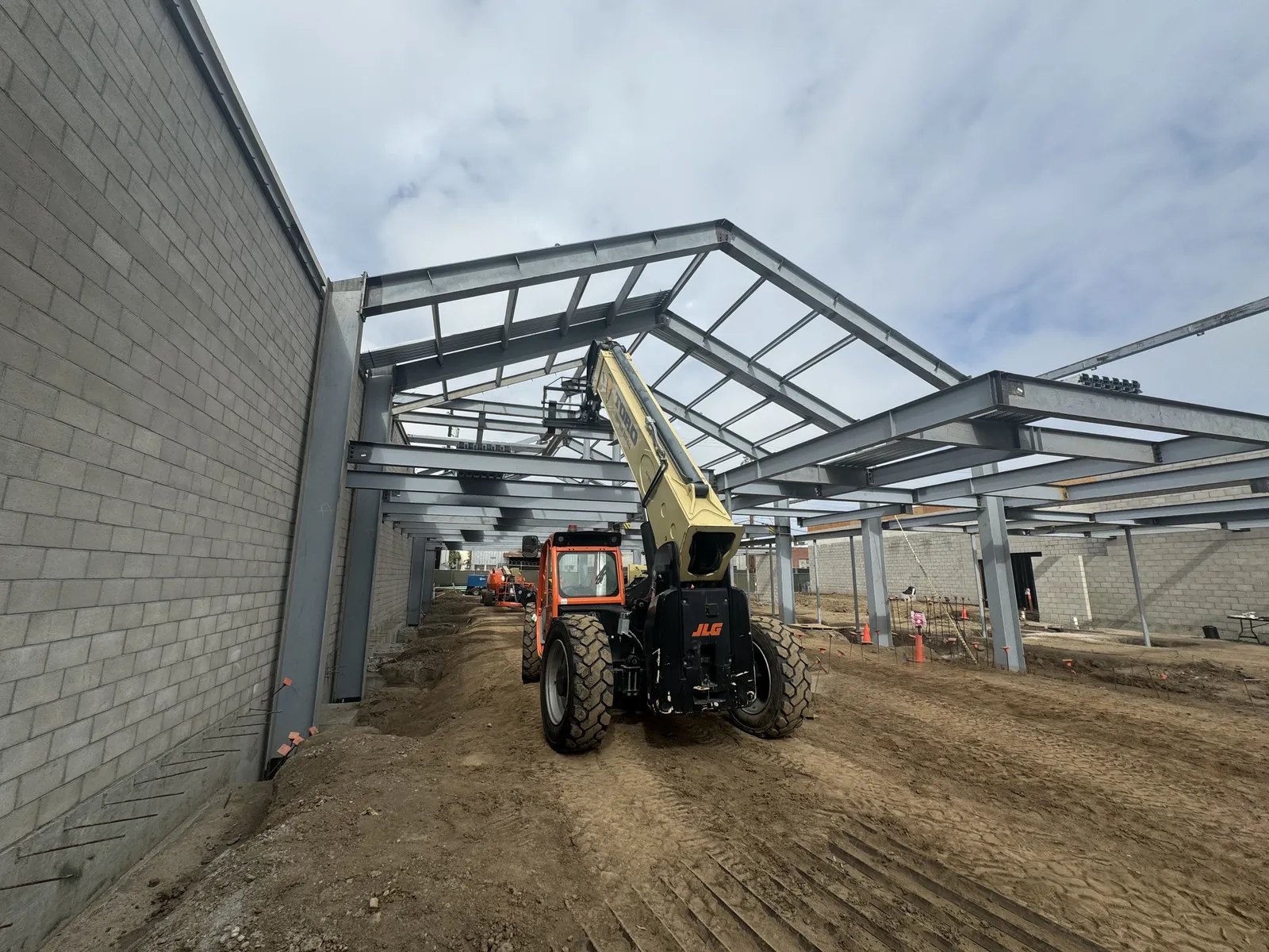 A steel frame going up beside a block wall, with a telehandler on the graded site