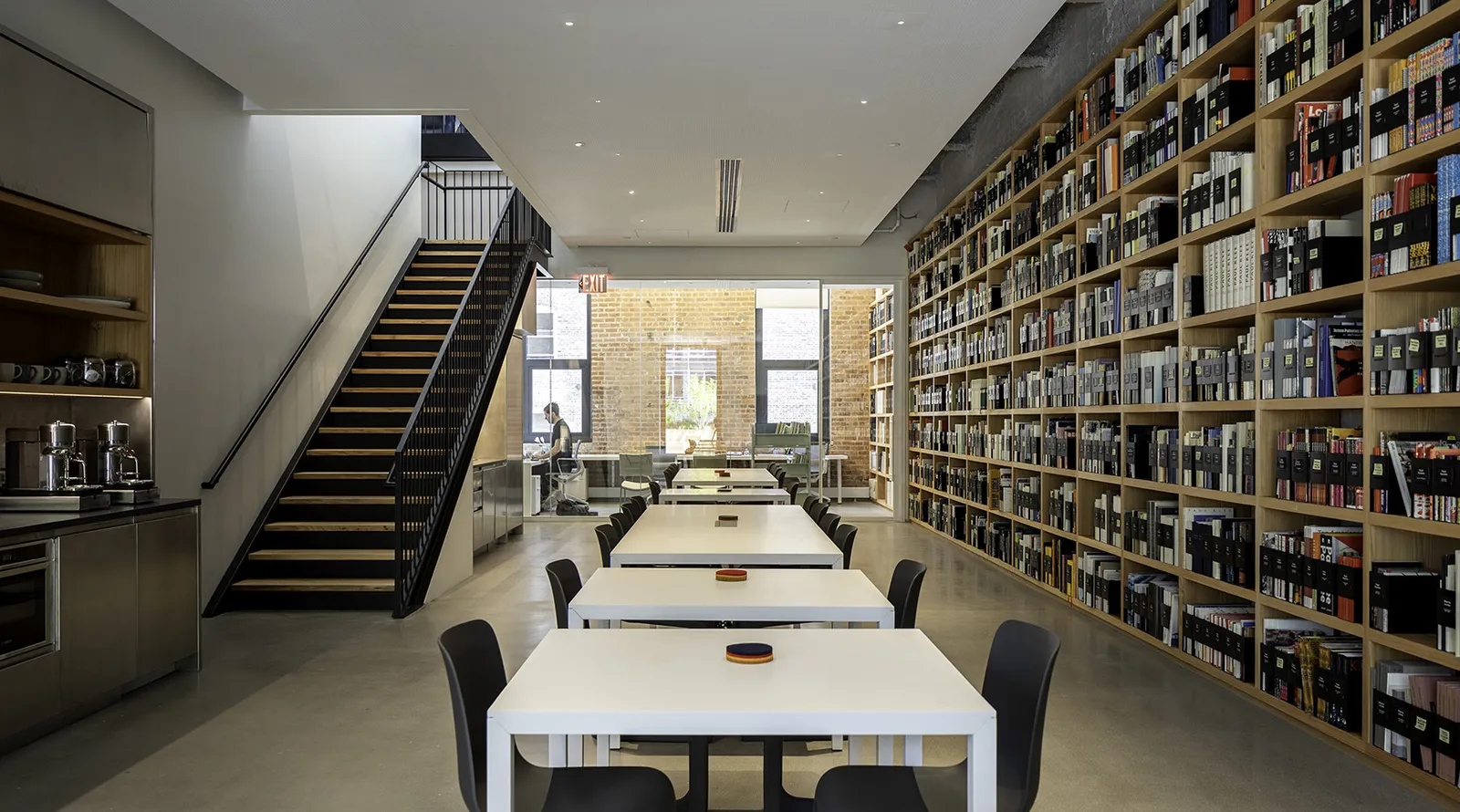 A long table beside a wall of bookshelves and a stair